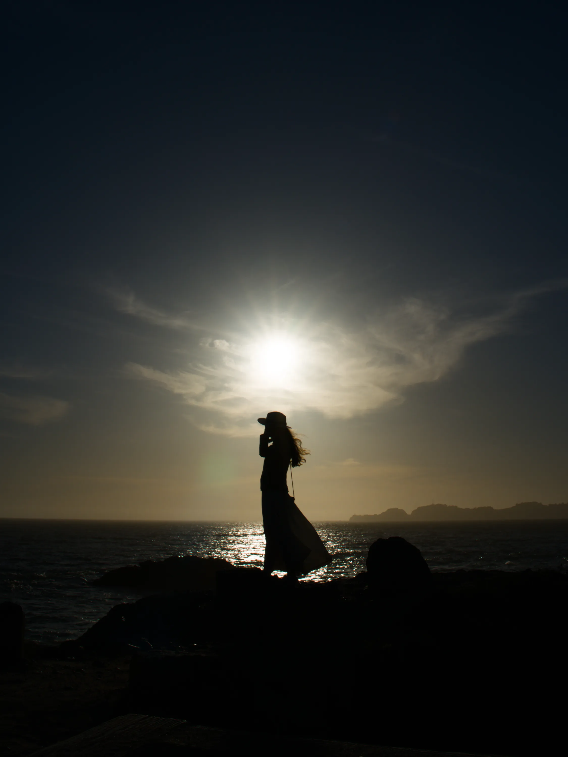 A womans black silhouette against the sun on a beach