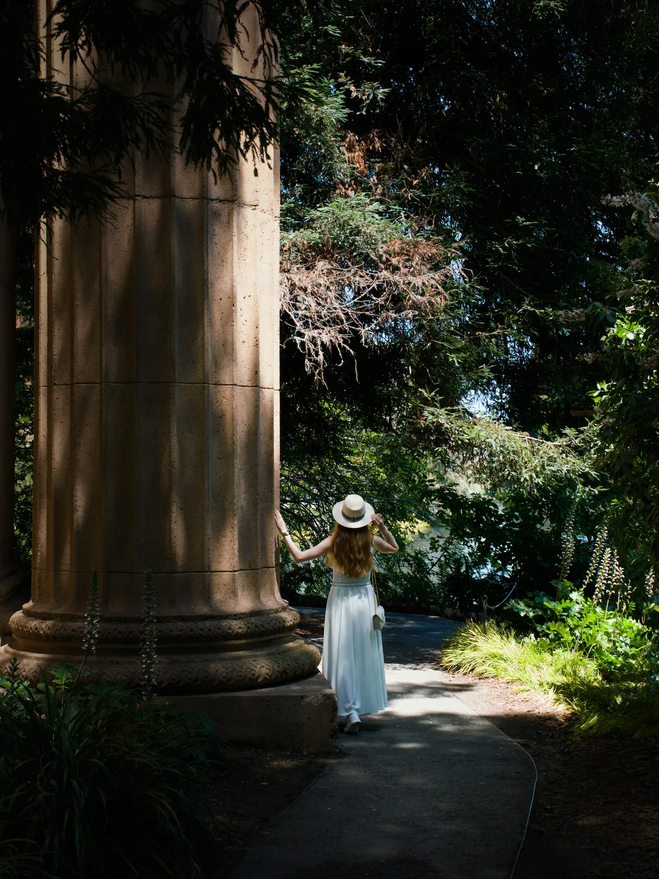 A woman in a white dress standing next to a monumental Greco-Roman column