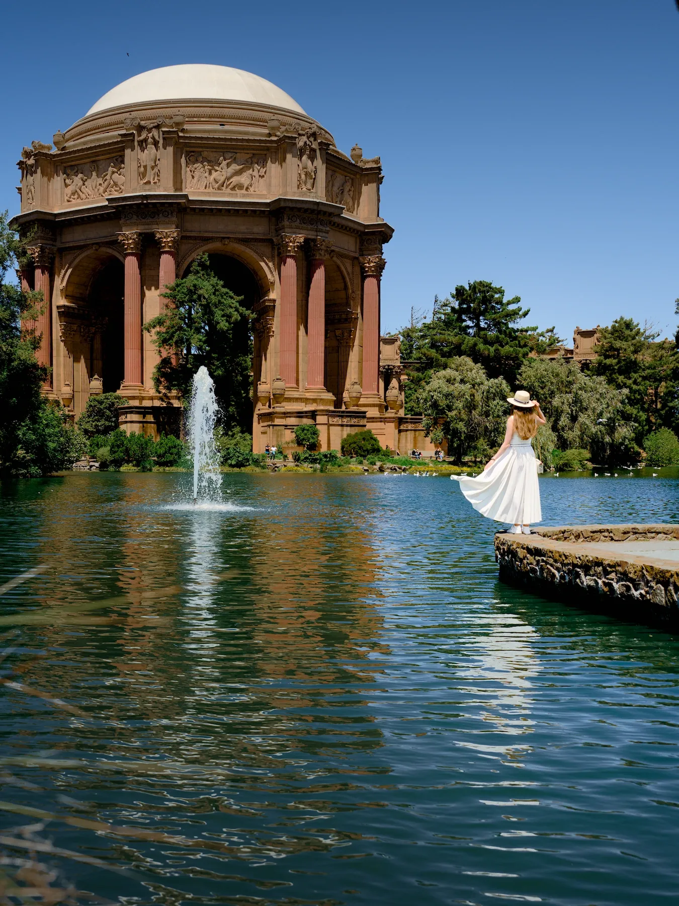 A woman in a white dress standing near the massive Greco-Roman rotunda at the Palace of Fine Arts